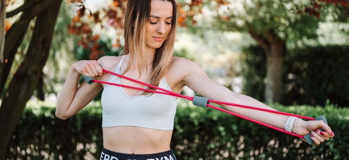 Fit woman using a resistance band for exercise in a sunny outdoor setting.
