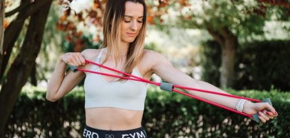 Fit woman using a resistance band for exercise in a sunny outdoor setting.